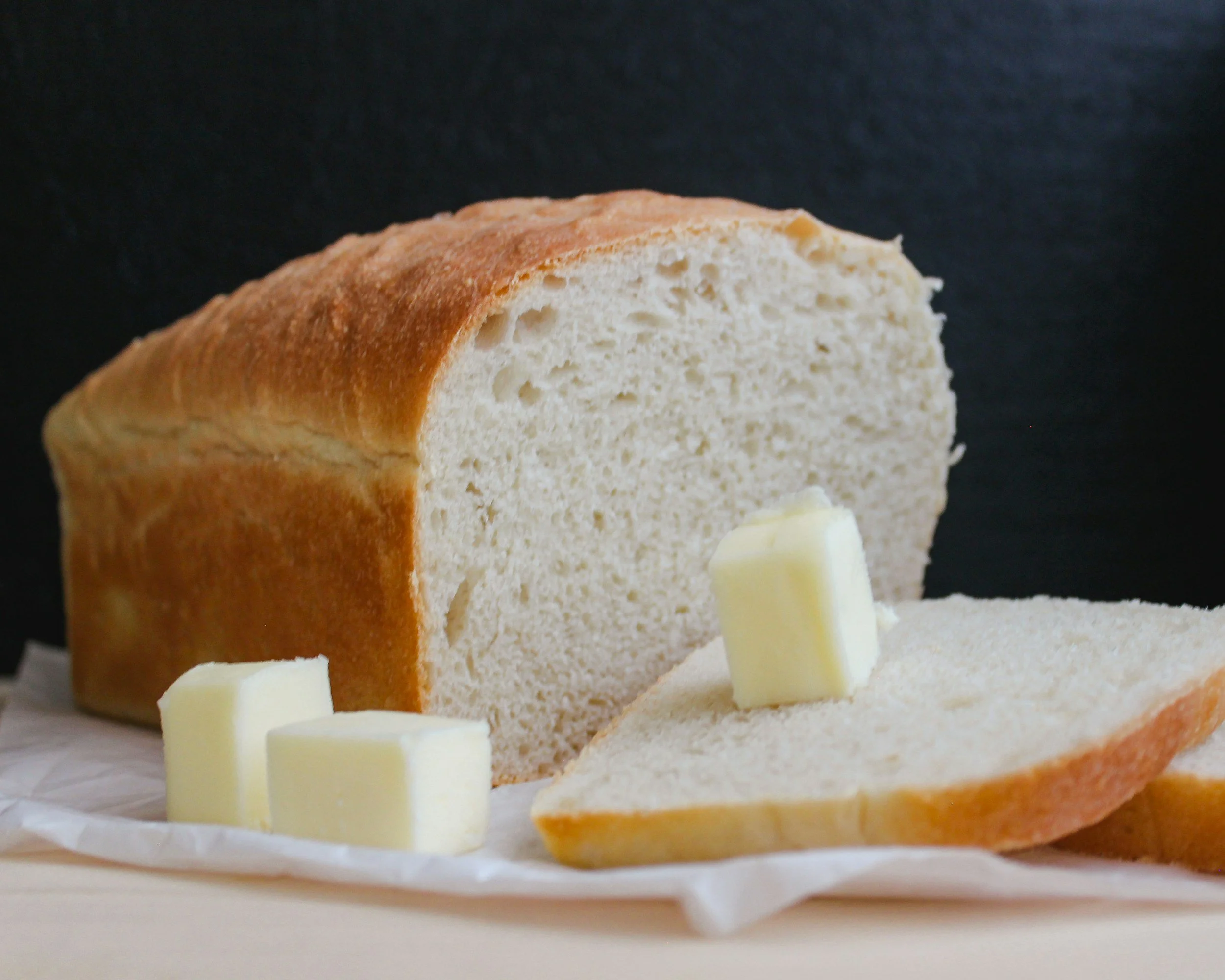 Loaf of white bread with sliced pieces and butter on top