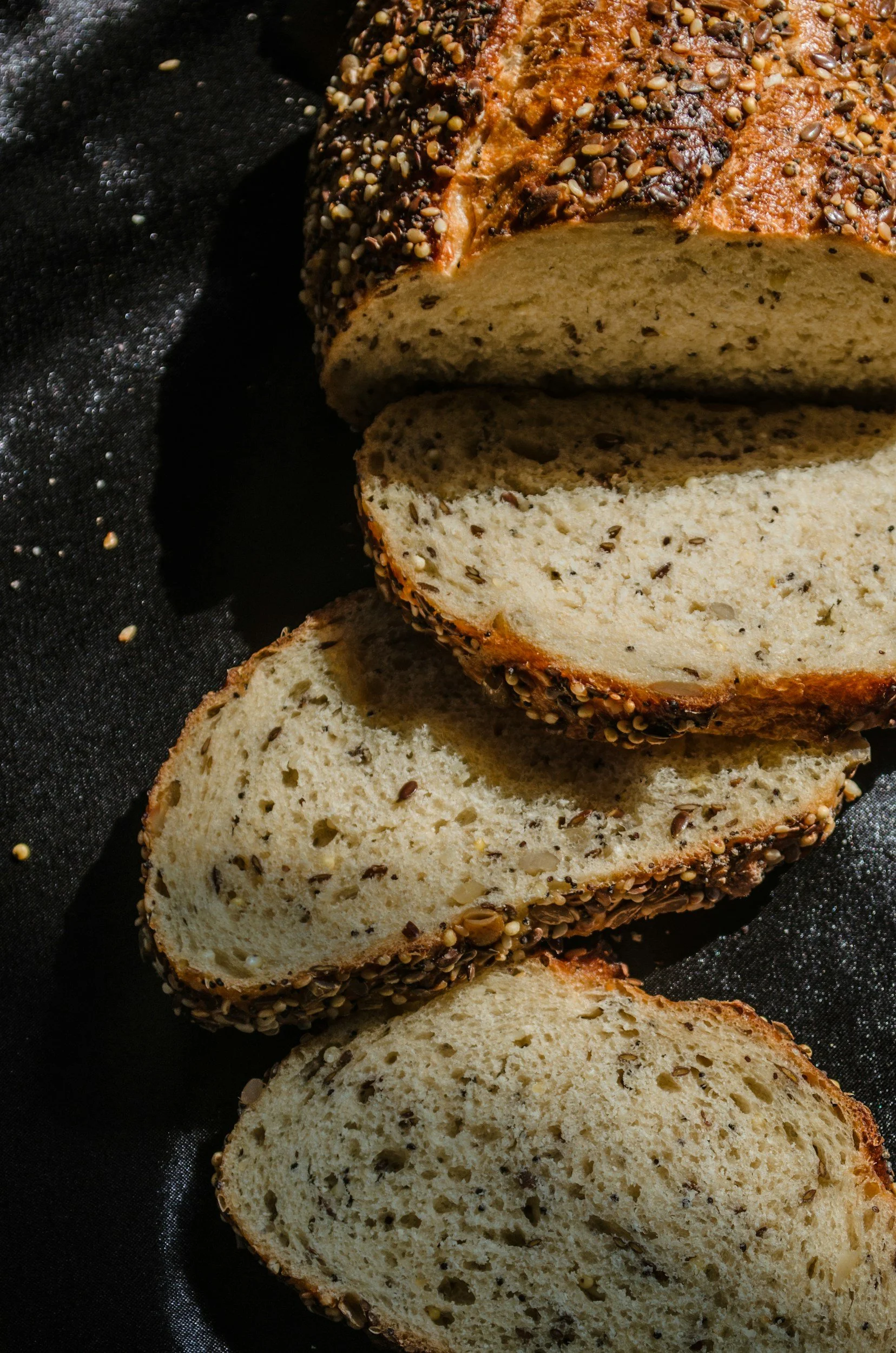 Sliced loaf of bread with seeds on the crust, resting on a black cloth.