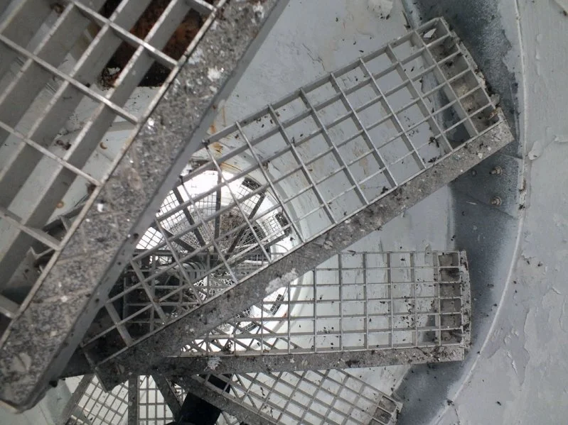 A close-up view of two metal grates or vents in a structural, industrial setting, with dirt and debris on and around them.