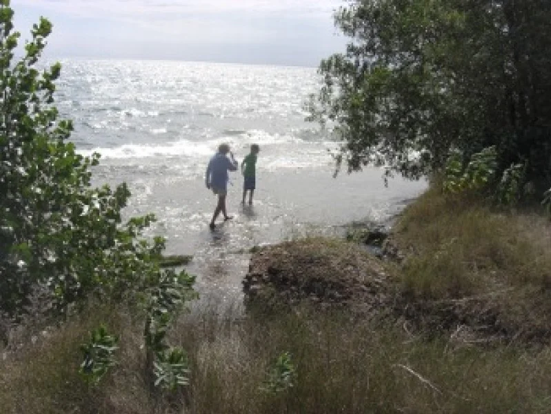 Two children standing at the shoreline by trees, with snow and ice on Lake Superior in the background.