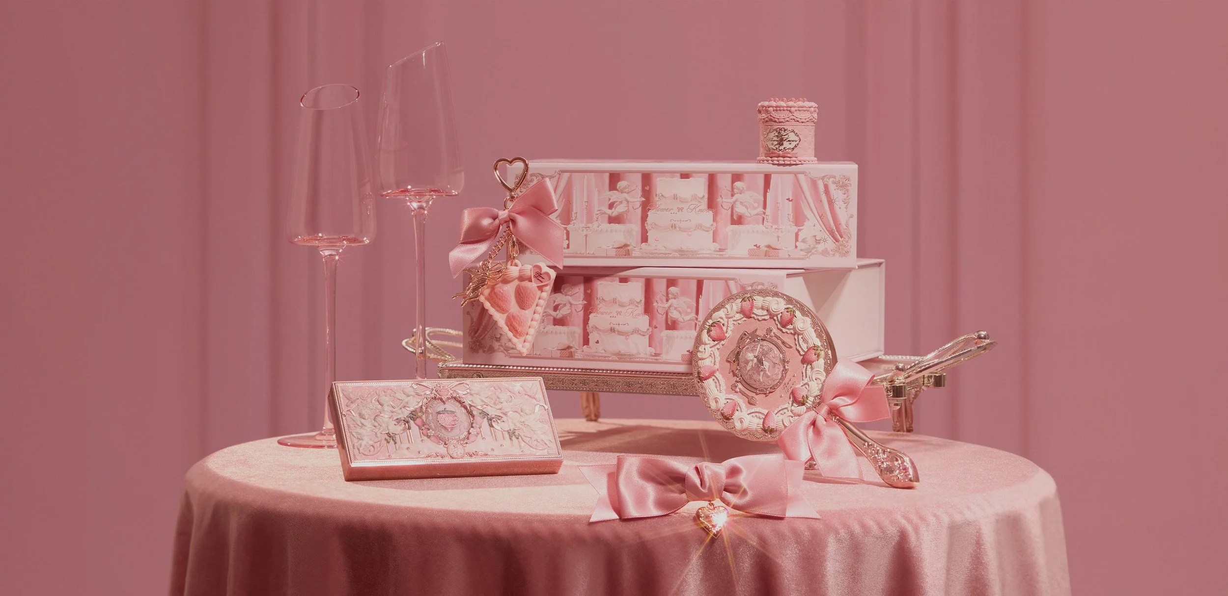 An elegantly styled flat lay of vintage-inspired pink makeup and coquette accessories featuring ornate cherub palettes, satin bows, and delicate glassware on a velvet tablecloth for a luxurious Princesscore aesthetic.