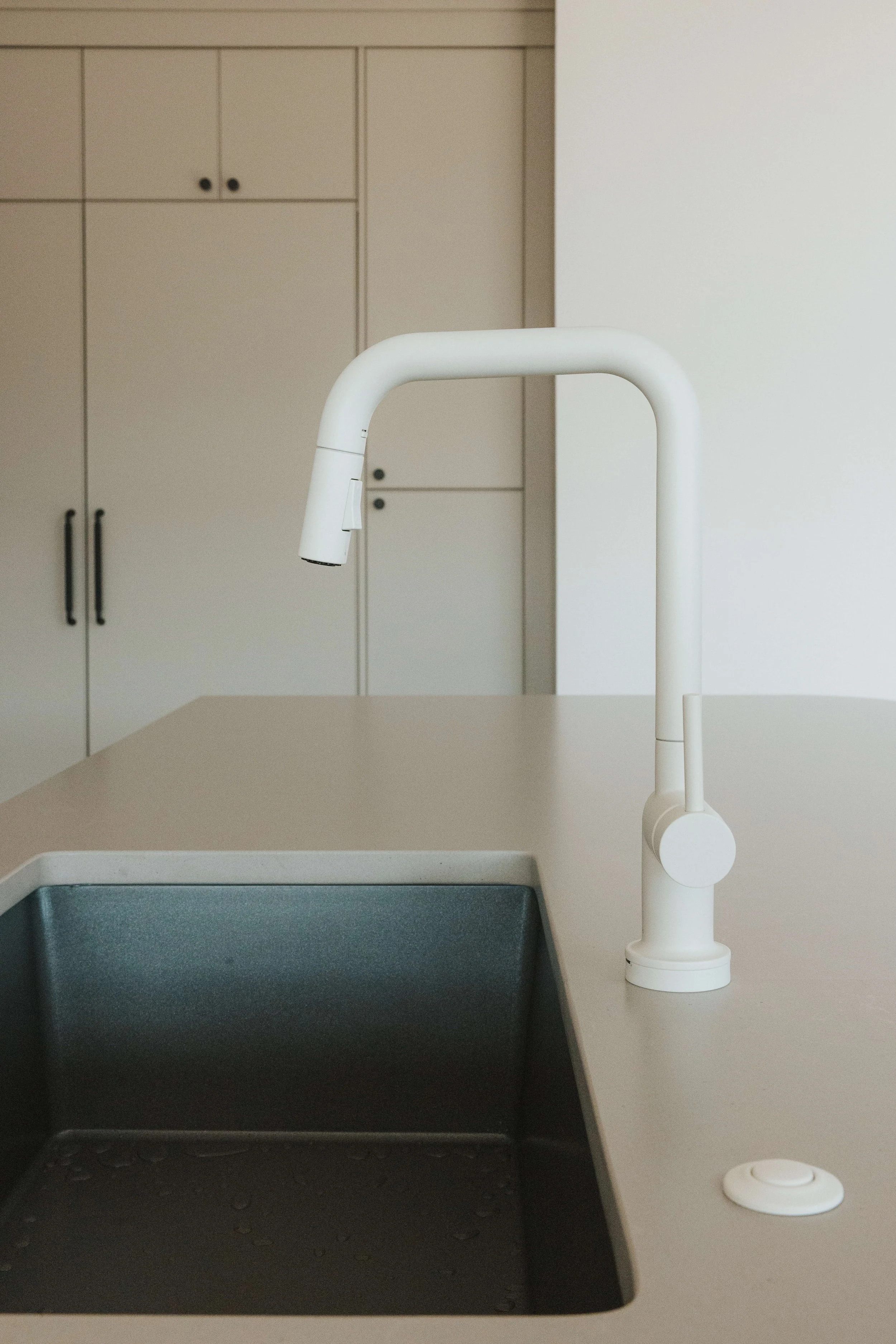 A white kitchen faucet over a black sink on a white countertop with a cabinet in the background.