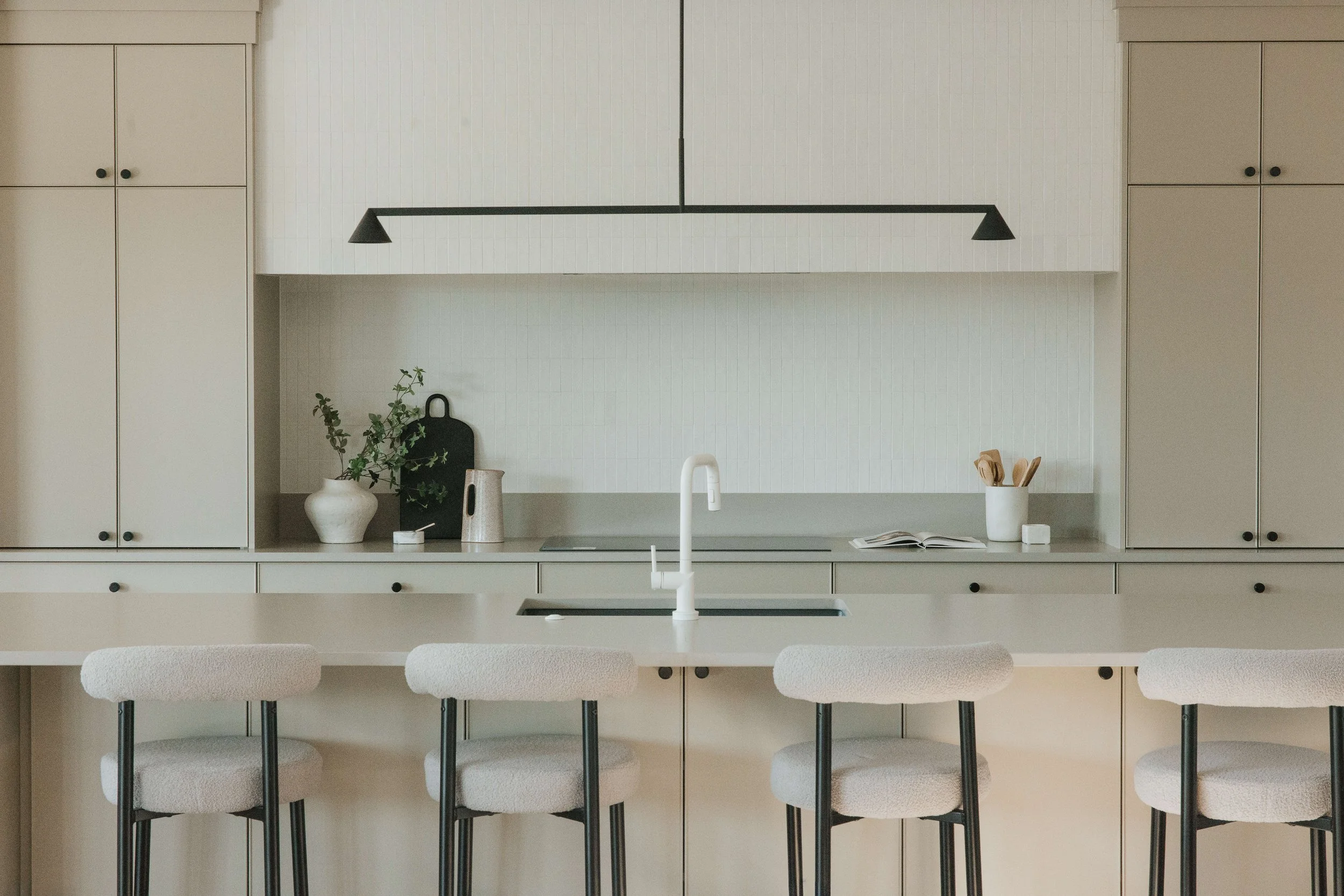 Modern kitchen with white cabinets, a white countertop, and a black hanging light fixture, with barstools at the counter.