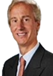 A smiling man in a dark suit, white shirt, and pink tie.