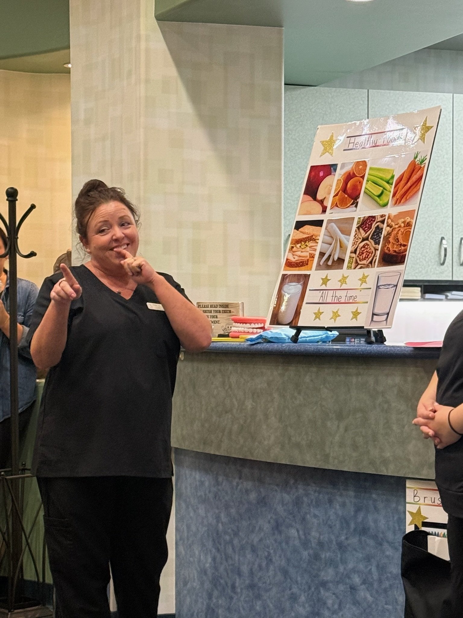 Staff member gesturing beside a poster of healthy foods and a model mouth on a counter