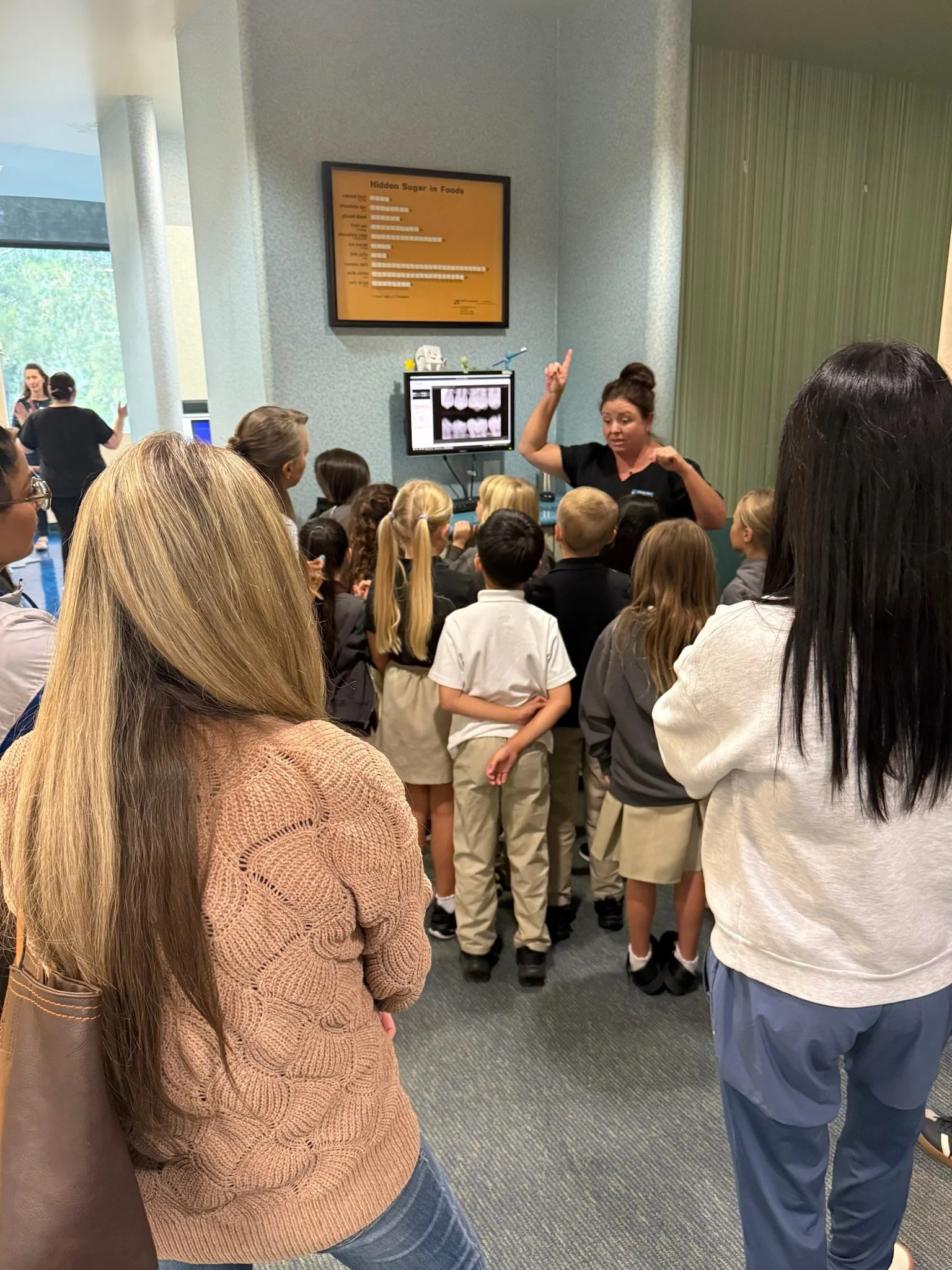 Adult speaking to a group of children gathered around a monitor displaying dental images