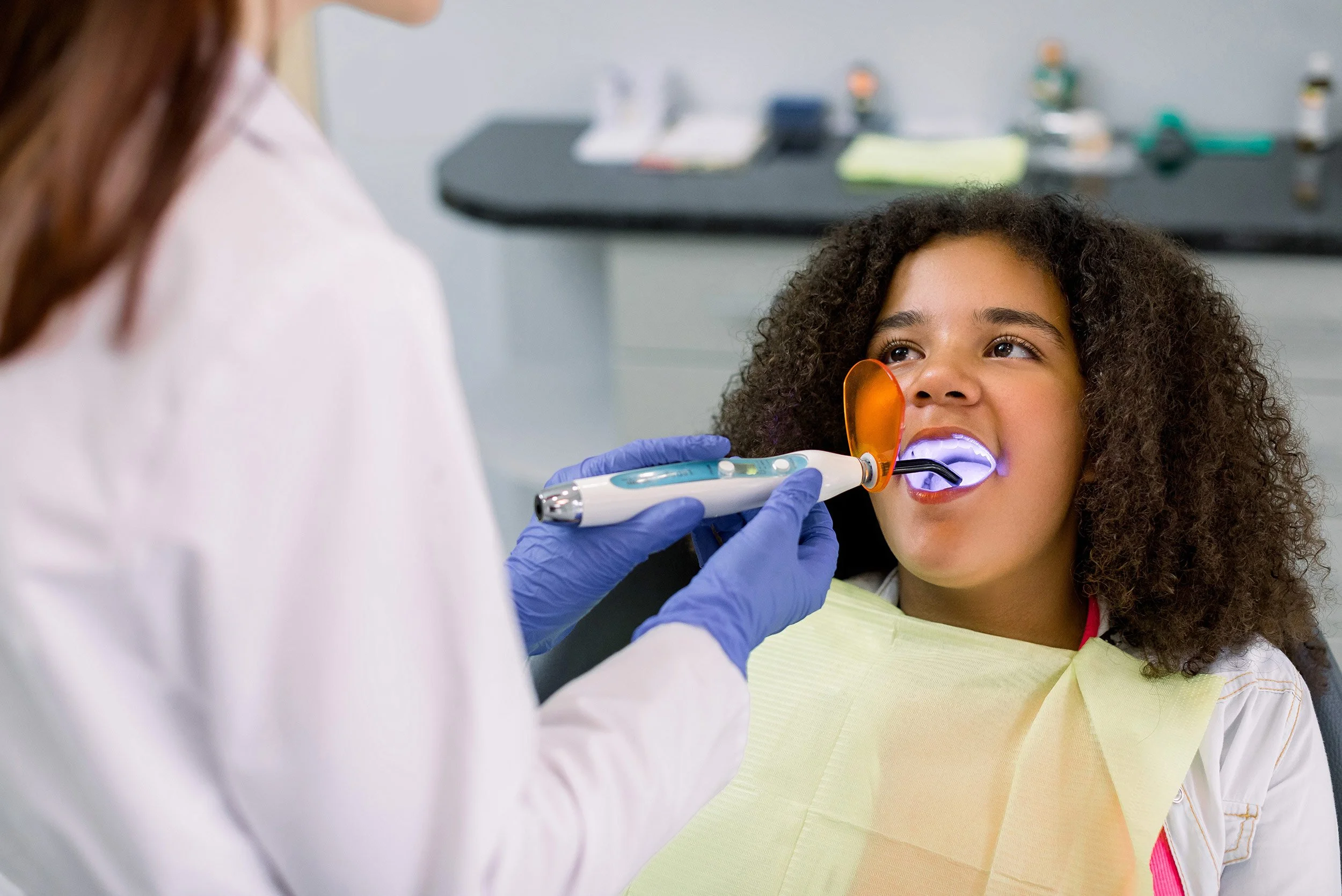 young girl getting sealants on her teeth with the sealant tool being used by her dentist