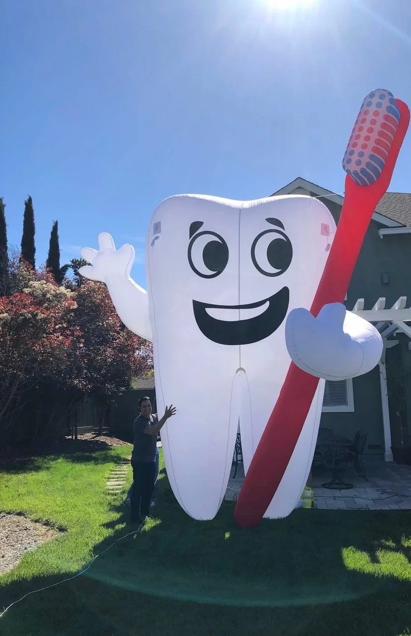 Giant inflatable tooth holding a large toothbrush on a sunny lawn