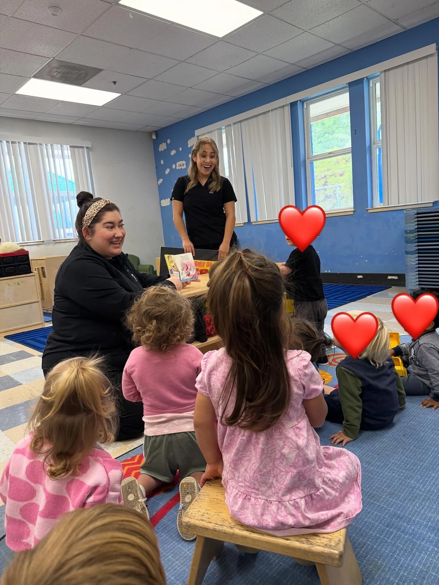 Adults reading a children’s book to a group of young kids seated on a classroom rug
