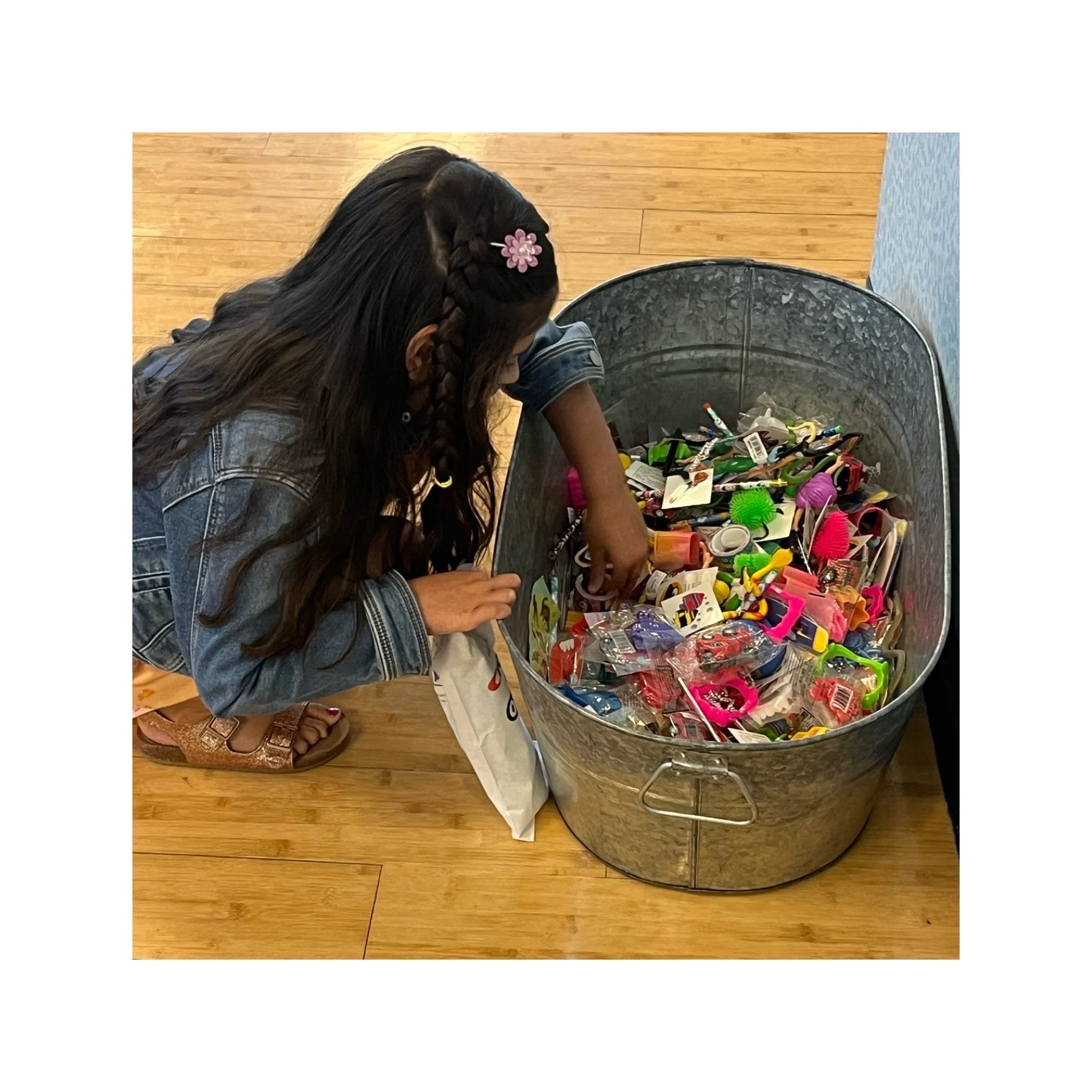 Child reaching into a large metal bin filled with small toys and prizes