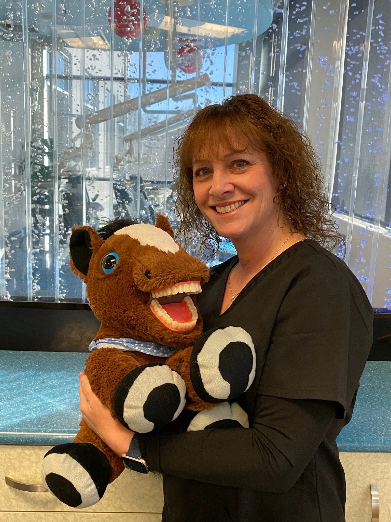 Staff member smiling while holding a plush horse in a dental office