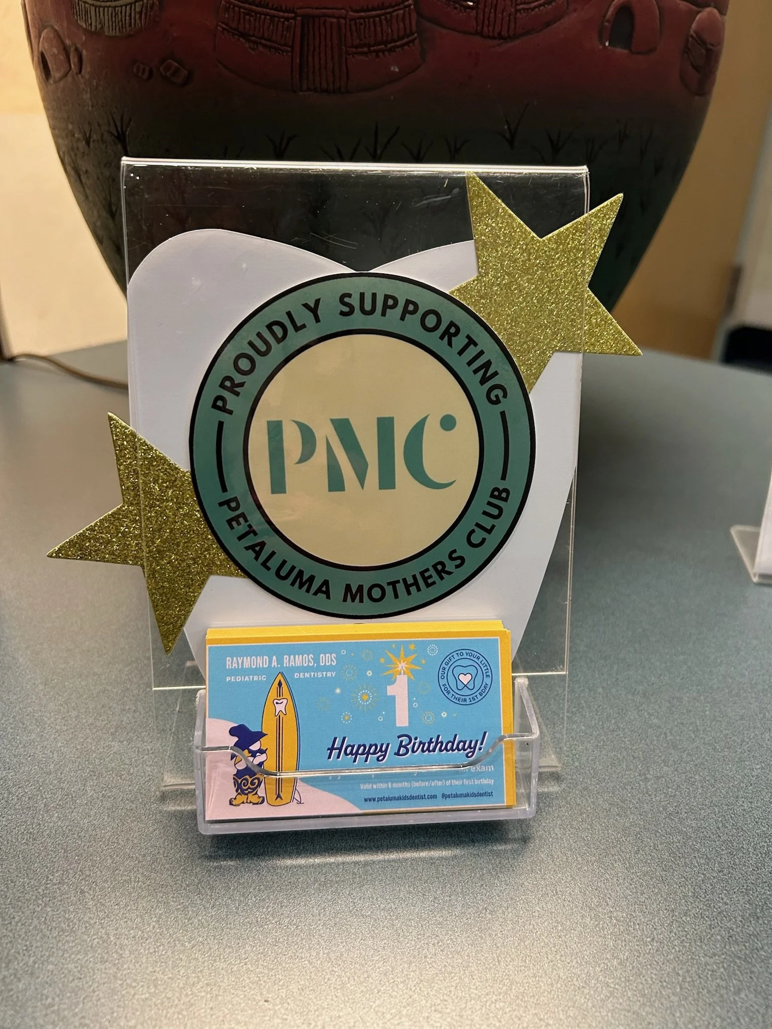 Display with a ‘PMC Petaluma Mothers Club’ sign and a ‘Happy Birthday!’ card in a holder