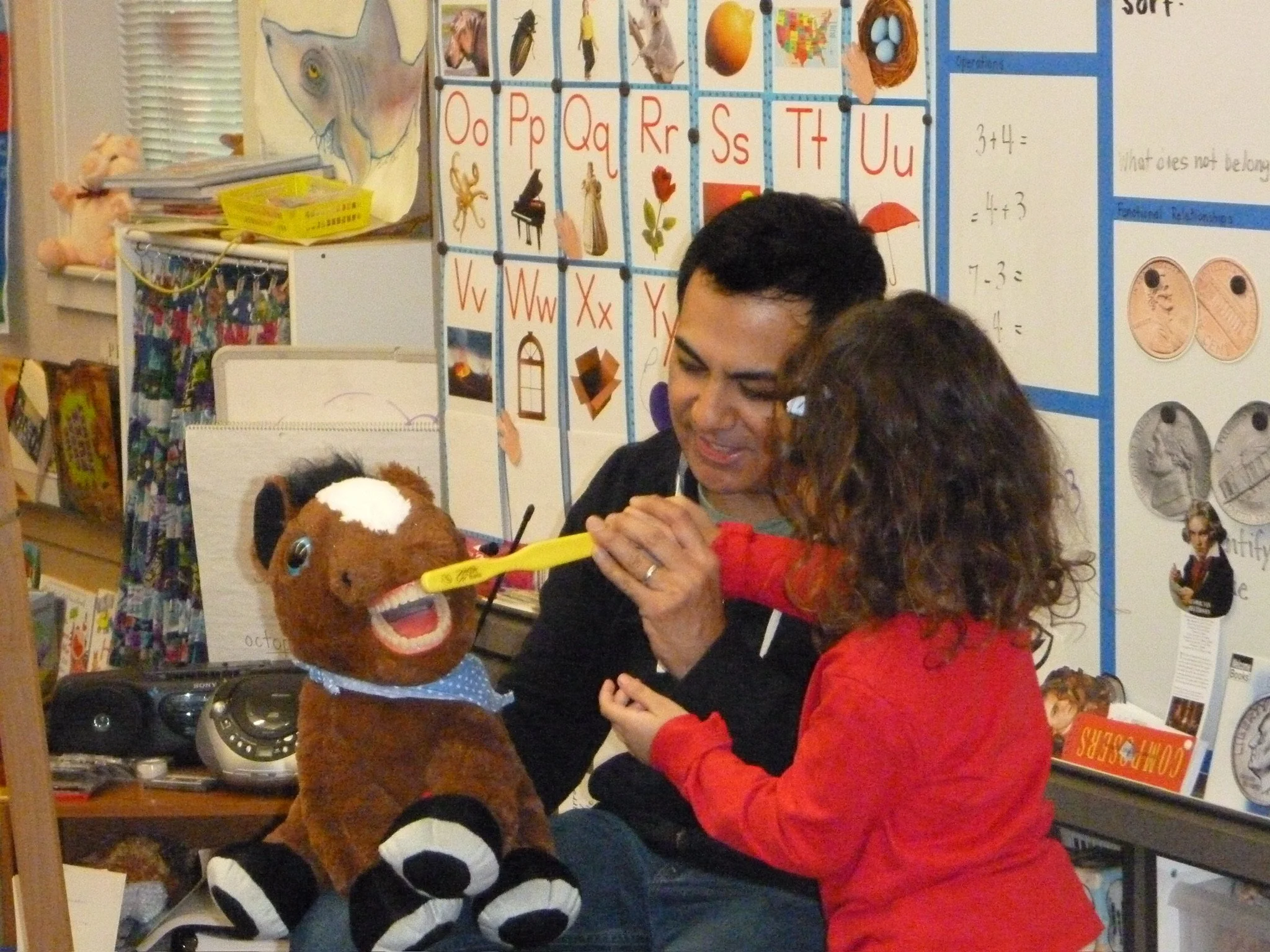 Dr. Ray in a children's calssroom showing a little girl how to brush teeth properly using a stuffed horse with human teeth as an example