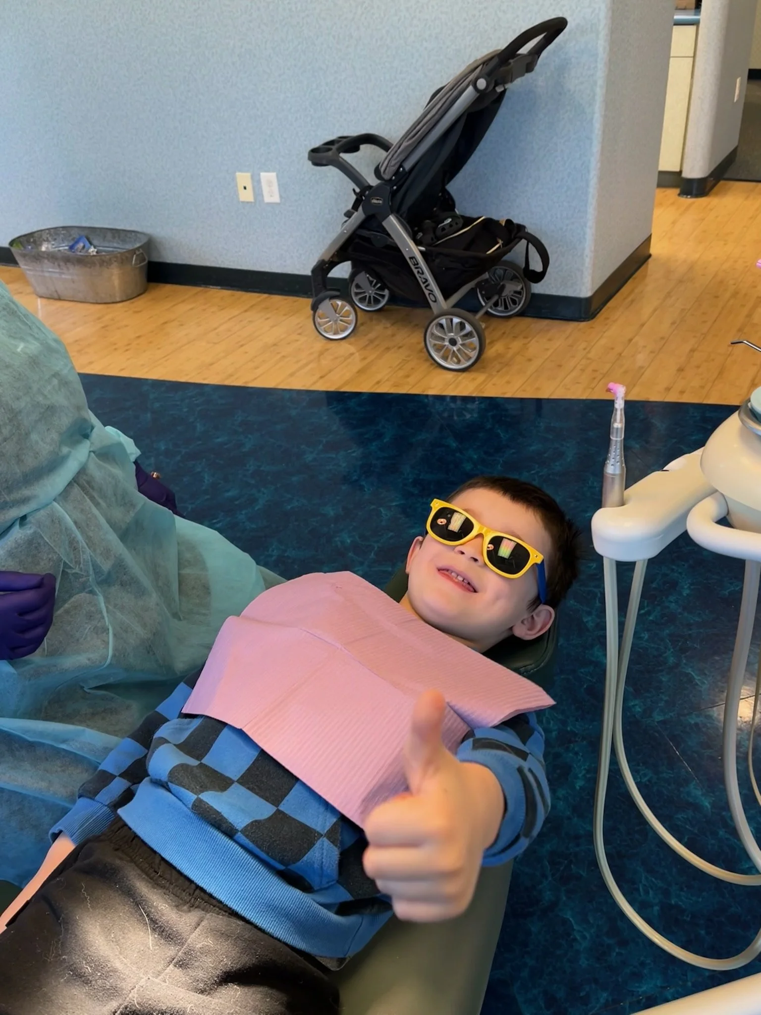 Child in a dental chair wearing sunglasses and giving a thumbs-up