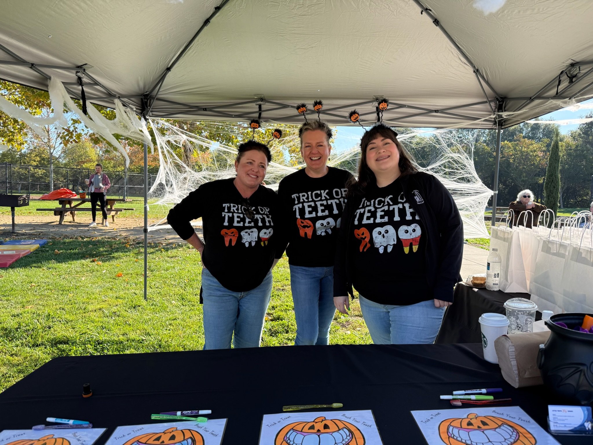 Three people smiling under a canopy table decorated for Halloween