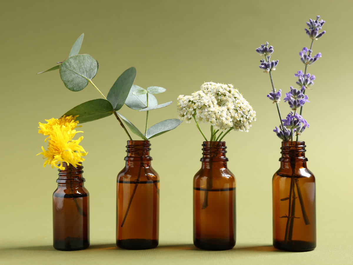 Four amber essential oils bottles are lined up with a different flower in each.