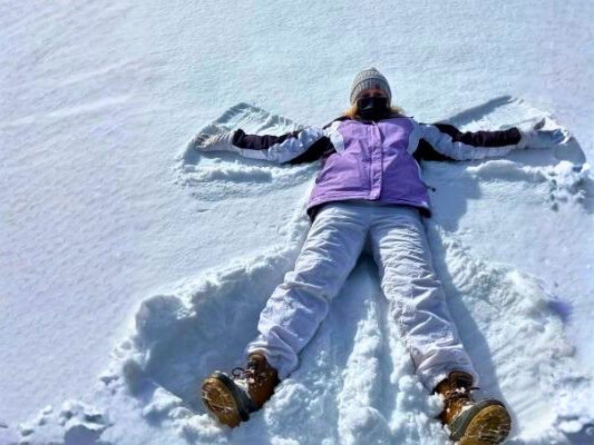 A woman bundled in winter-wear makes a snow angel in a crisp white blanket of snow