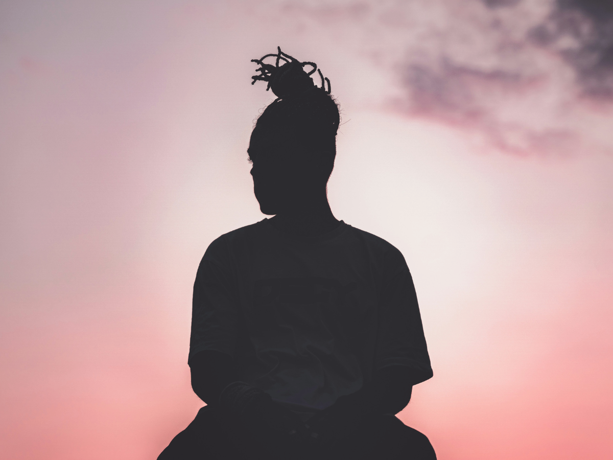 A woman sits in silhouette in front of a colorful sunrise.