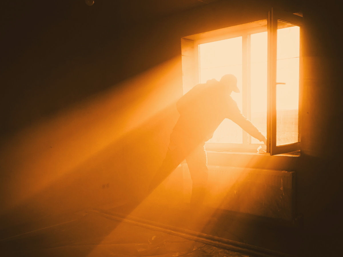 Sun rays pour through window at golden hour.  A man stands in the rays as he opens the window.