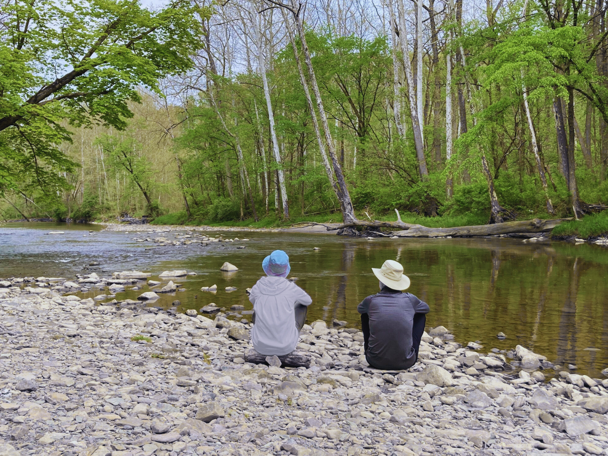 two people sit on a log, looking at the peaceful river