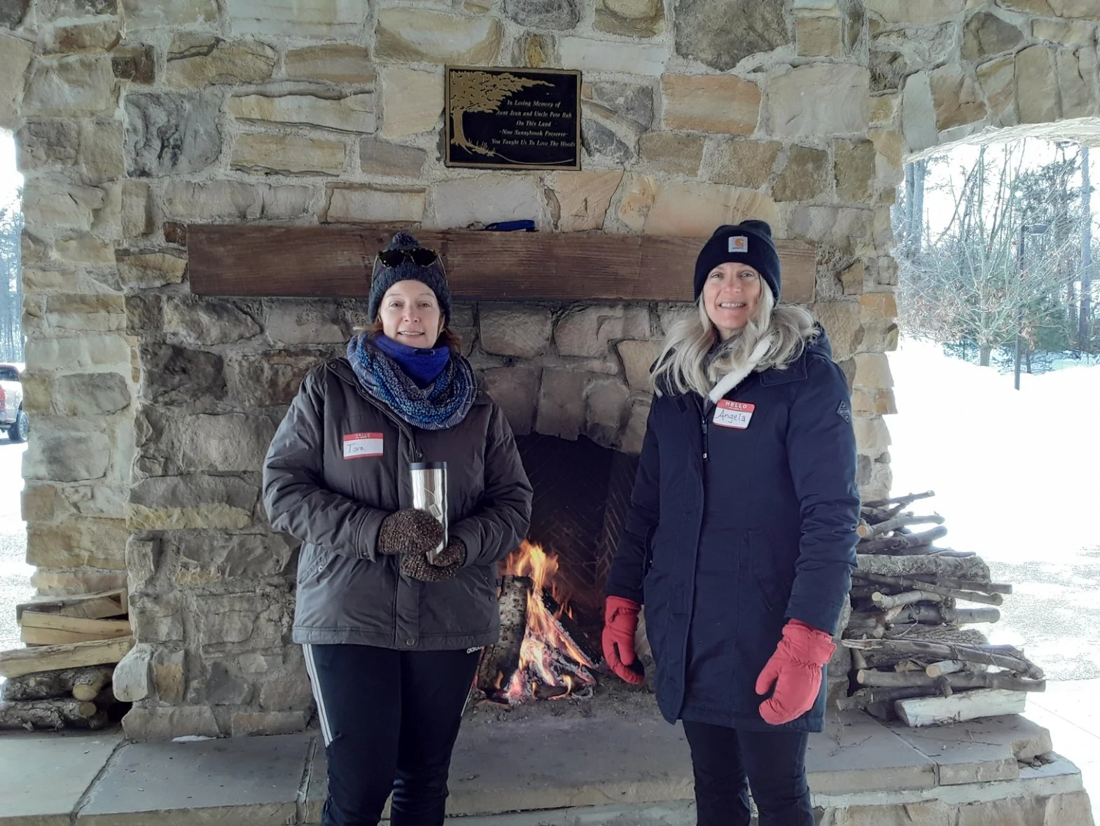 Two women stand before the fire at Sunnybrook Preserve on a bright winter day