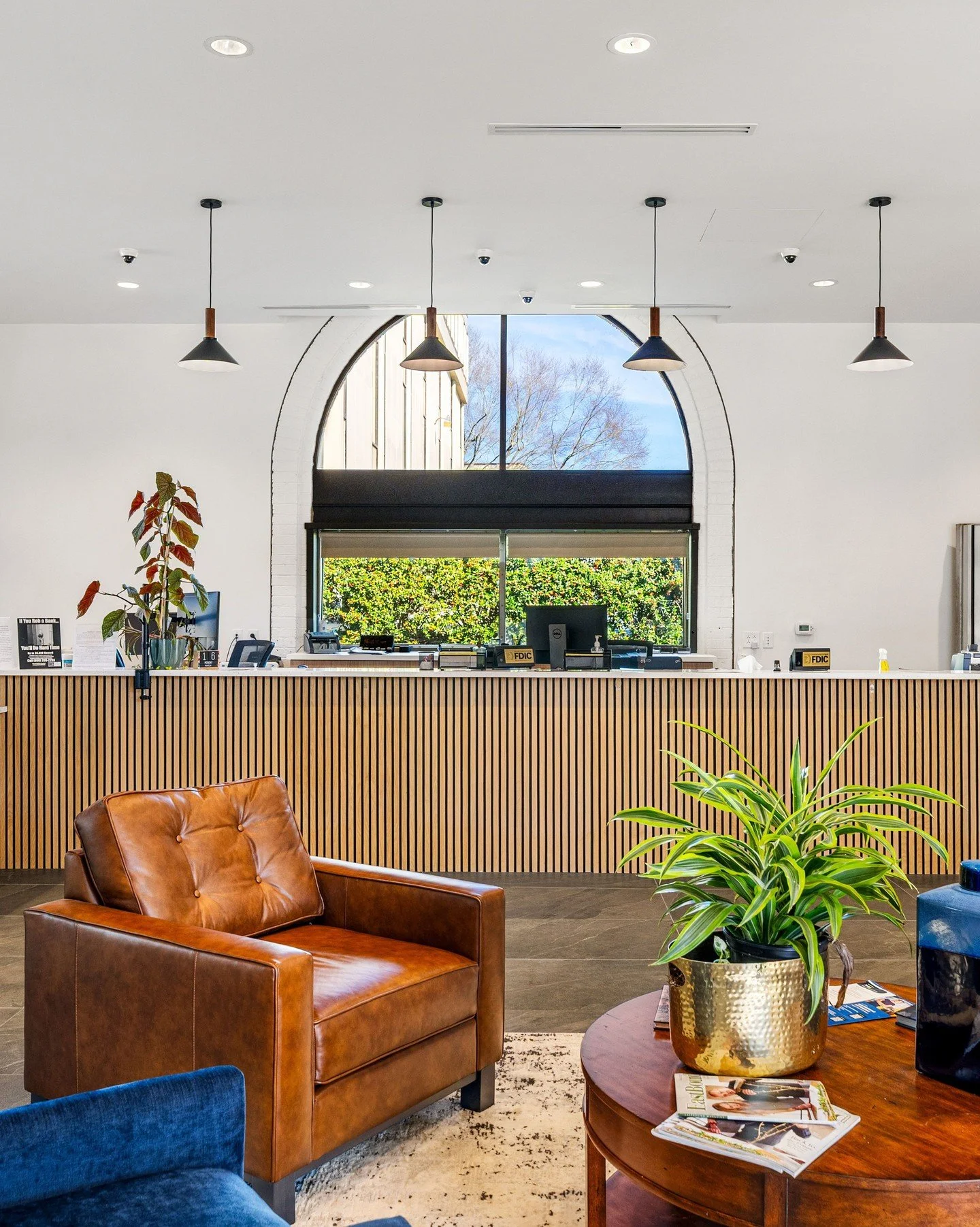 Inside Providence Bank the design emphasizes openness, natural light, and a warm, welcoming atmosphere. A custom wood slat front desk anchors the reception area, complemented by lounge seating and a palette of soft, neutral finishes. Outside, a serie