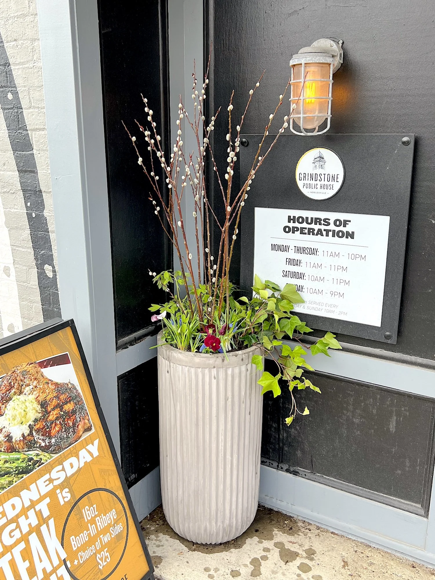 Fresh, vibrant spring planters overflowing with seasonal blooms and lush greenery at Grindstone Public House in Noblesville, Indiana. These professionally designed outdoor planters feature a mix of colorful flowers, textured foliage, and natural elem