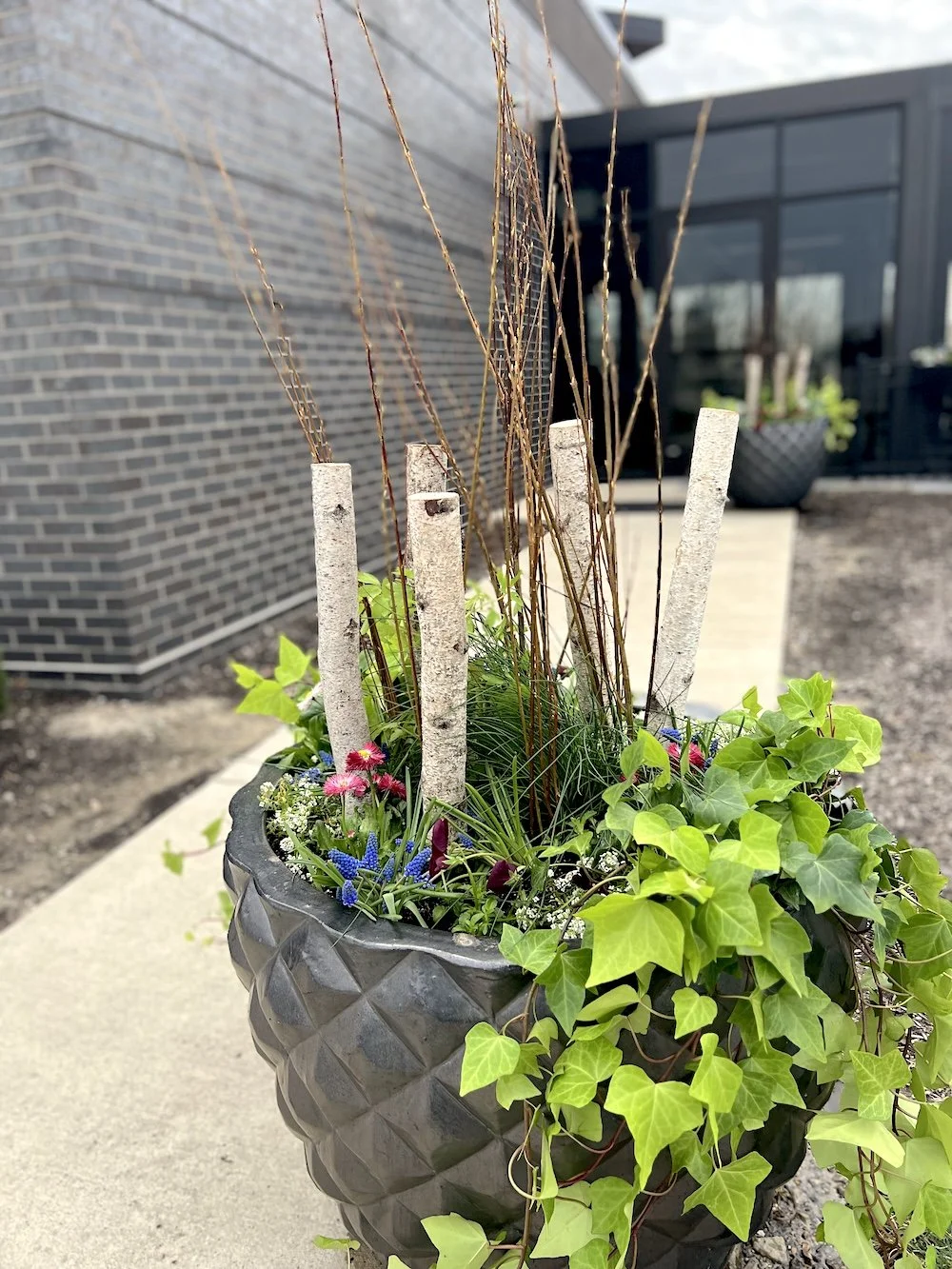Fresh, vibrant spring planters overflowing with seasonal blooms and lush greenery at Grindstone on the Monon in Westfield, Indiana. These professionally designed outdoor planters feature a mix of colorful flowers, textured foliage, and natural elemen