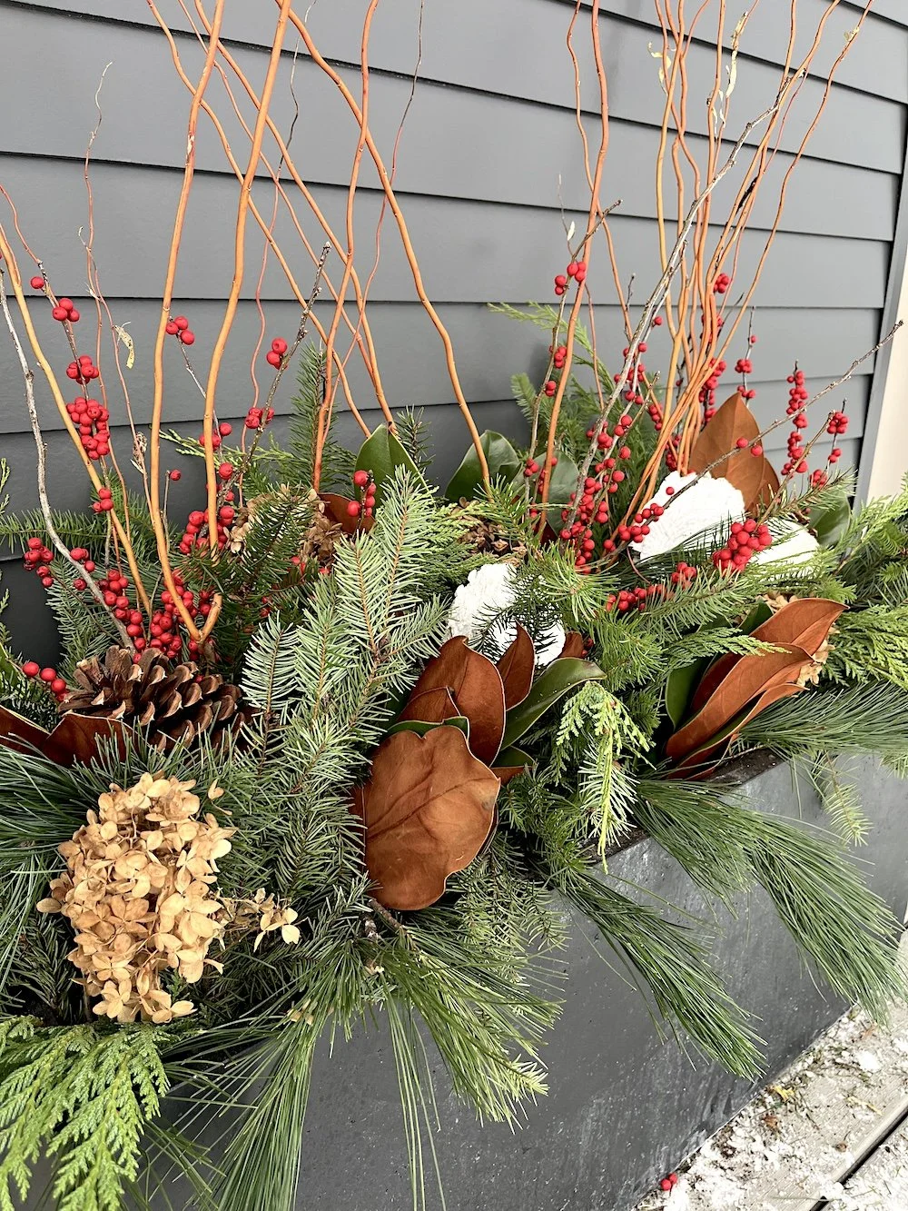 Elegant winter planters at MJC in Fishers, Indiana, featuring a seasonal mix of evergreen branches, pinecones, berries, and natural accents. These professionally designed outdoor containers bring texture, height, and festive charm to the space, perfe