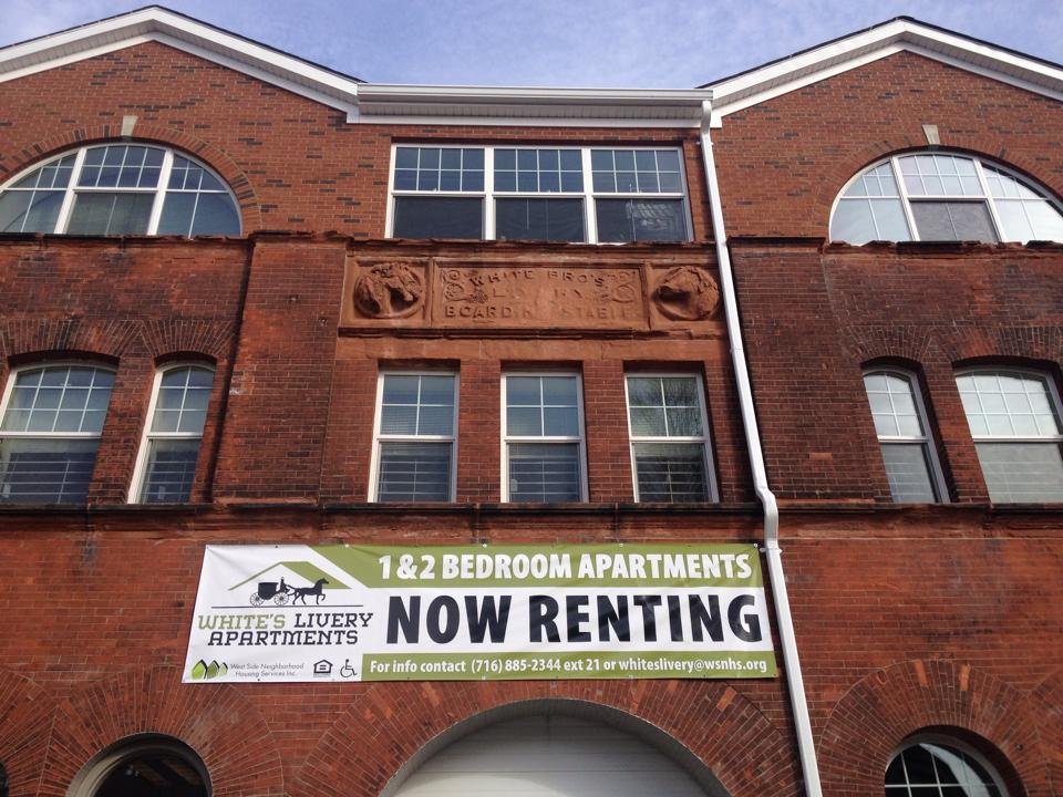 White's Livery underwent an adaptive reuse of its historic red brick building in Buffalo, NY. Here we see it with banner advertising 1 and 2 bedroom apartments for rent, labeled "White's Livery Apartments."