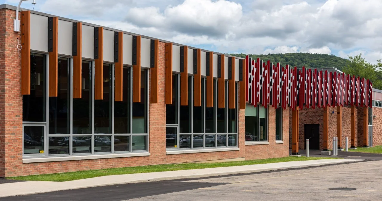 Modern building with brick exterior, large windows, wooden and striped red and white decorative panels.