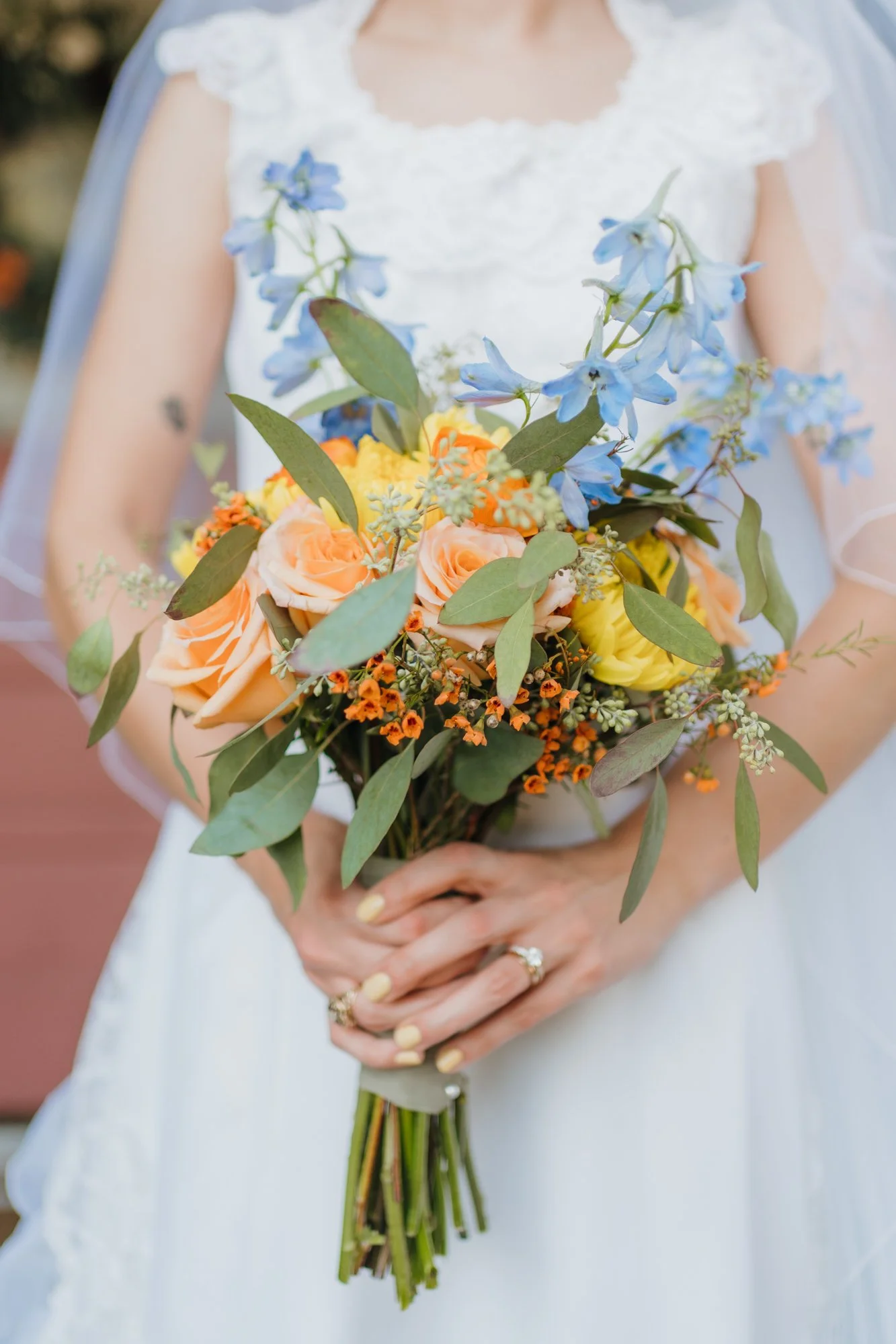 Zoe holds her orange, peach, and blue bridal bouquet.