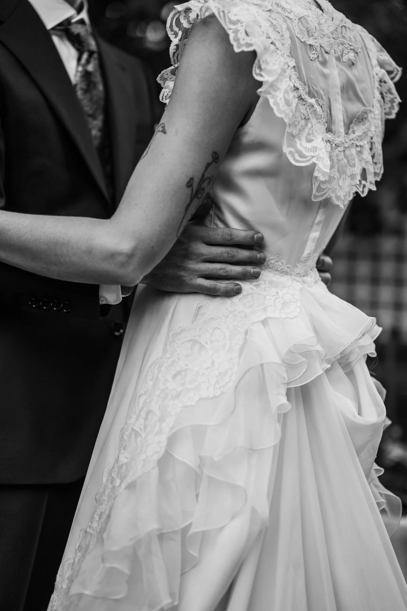 Black and white close up of Hunter's hand on Zoe's lace dress as they dance.