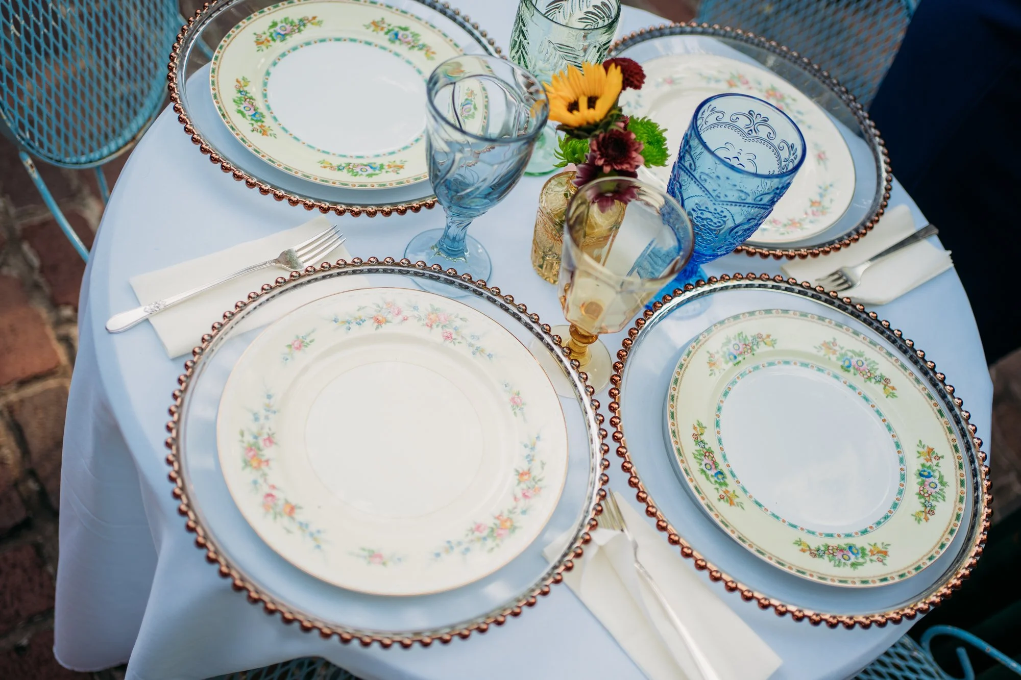 Vintage china plates and blue glasses on a round reception table.
