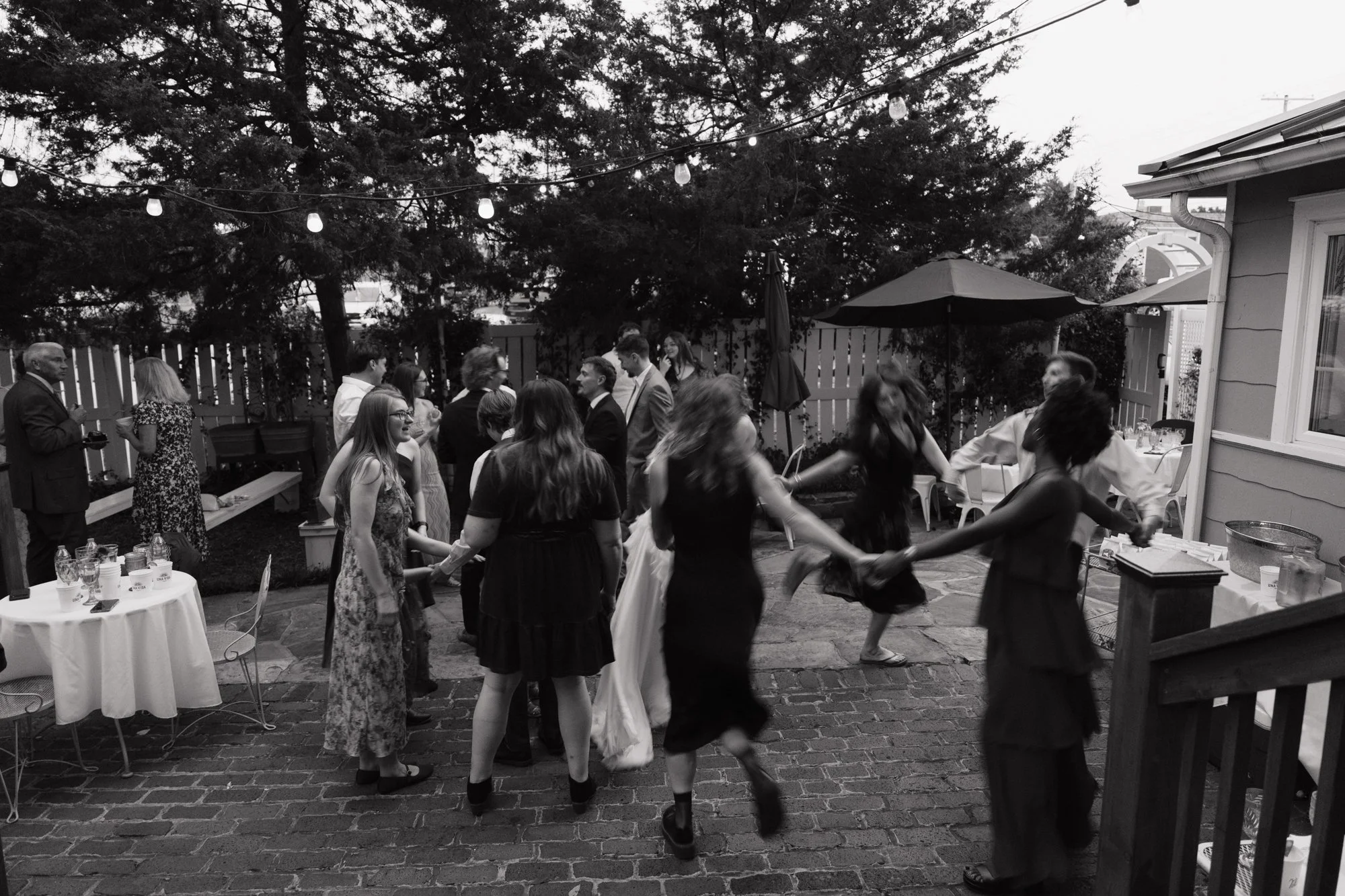 Guests dance in a circle in the backyard, in black and white.
