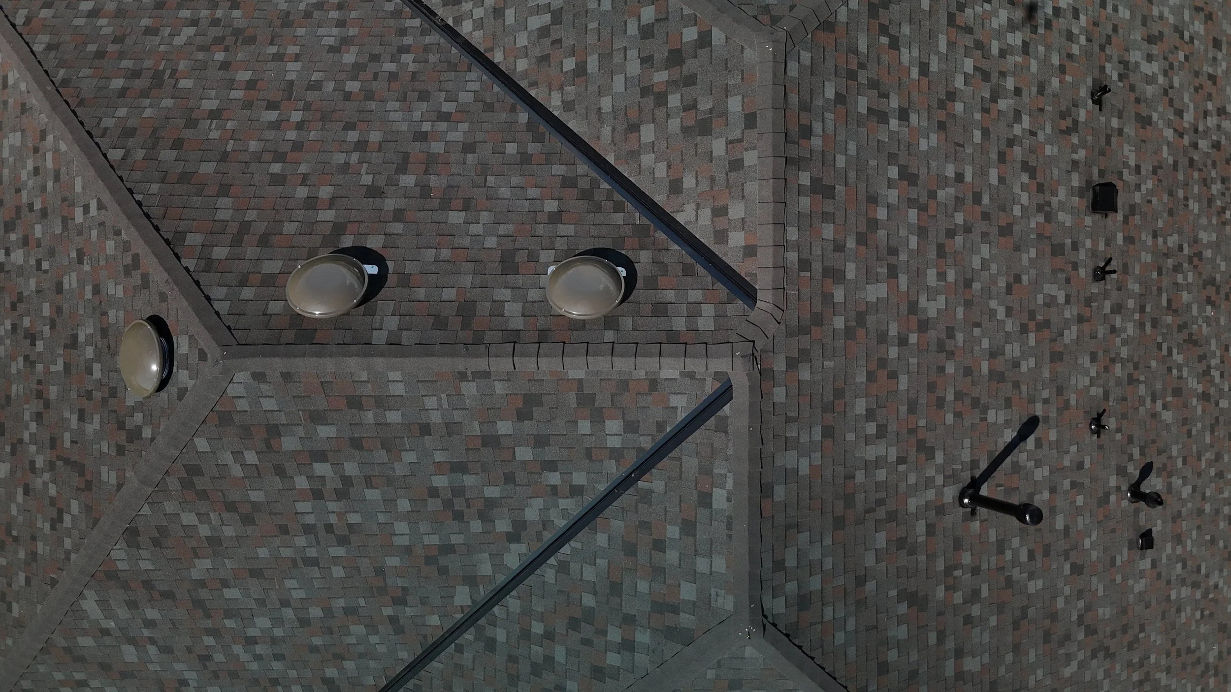 A brick building wall with four black metal lamps and three black vent pipes or exhaust outlets.
