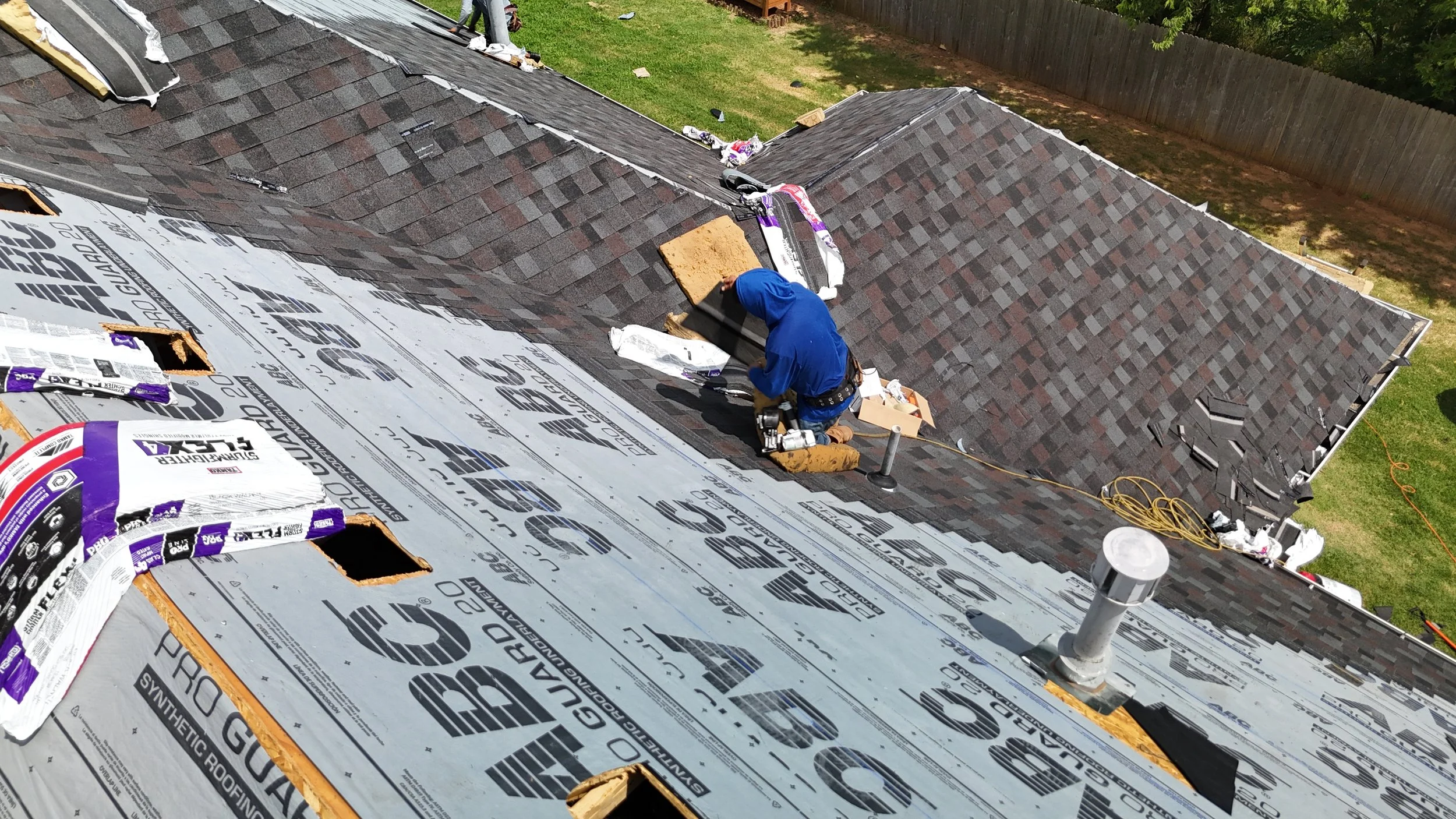 A person working on installing or repairing roofing shingles on a house's roof, with the roof partially covered in underlayment.