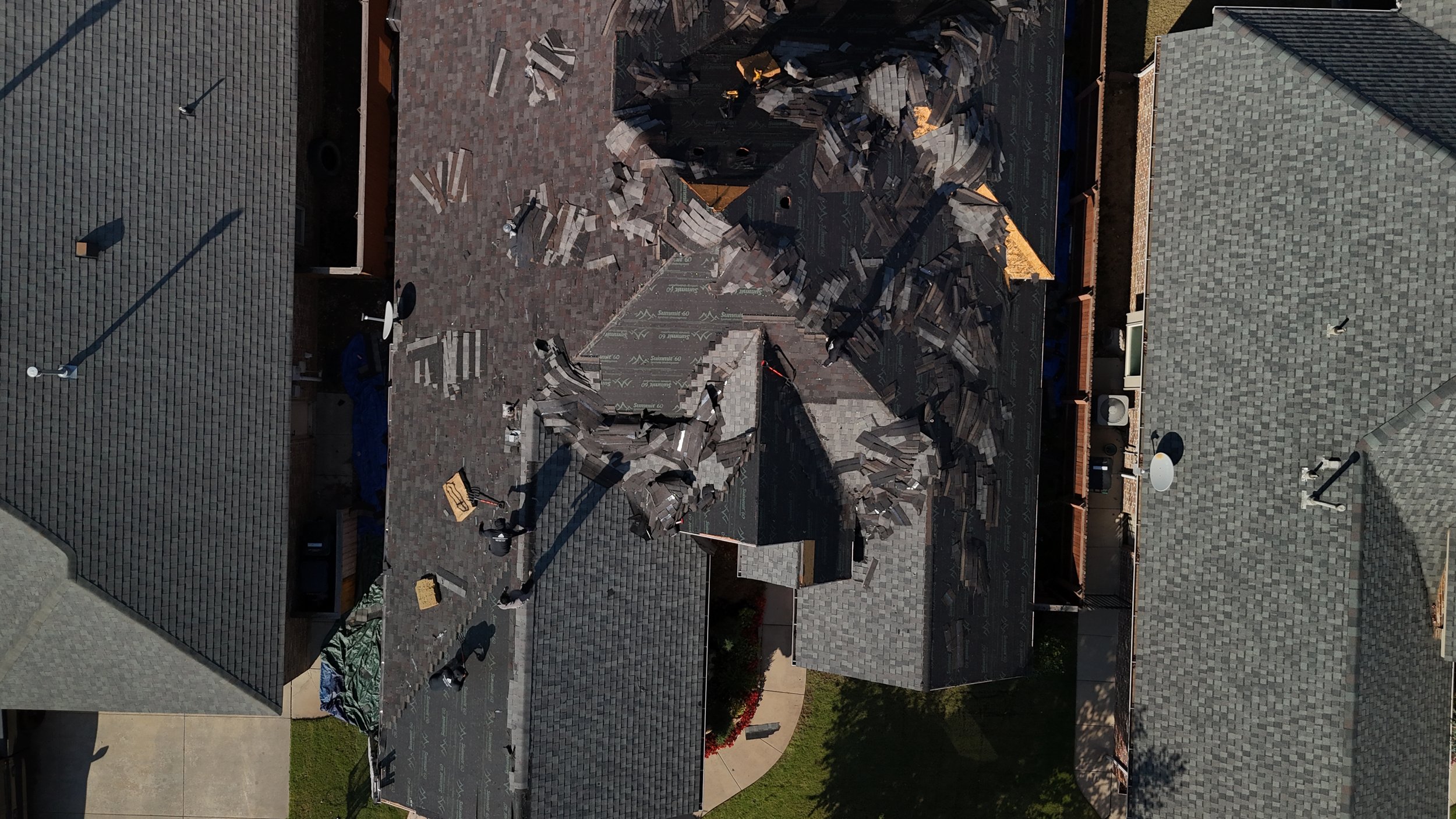 Aerial view of a house roof with shingles replaced, showing roof tiles and construction debris on top.