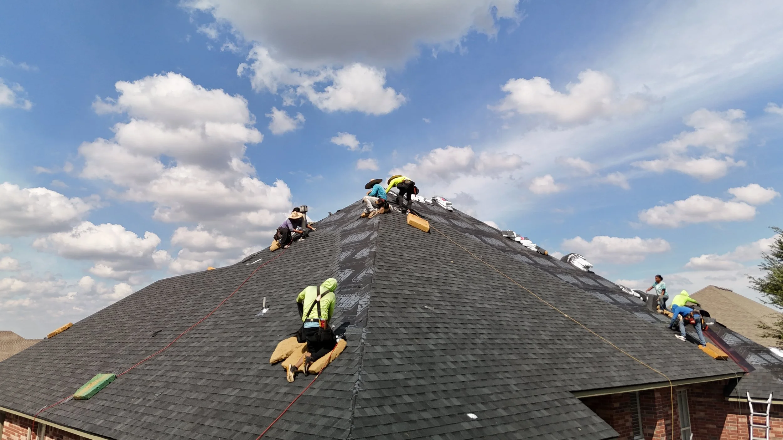 Construction workers installing or repairing roofing on a house under a partly cloudy sky.