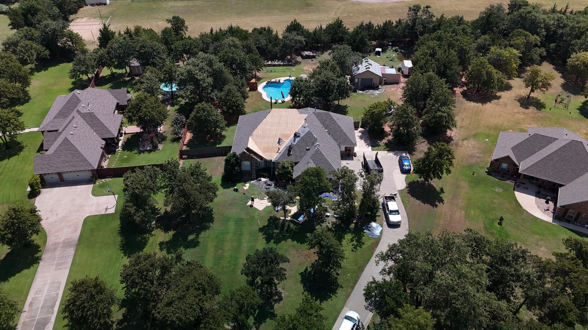Aerial view of a suburban neighborhood with several houses, trees, a swimming pool, and a backyard with ongoing construction or renovation.