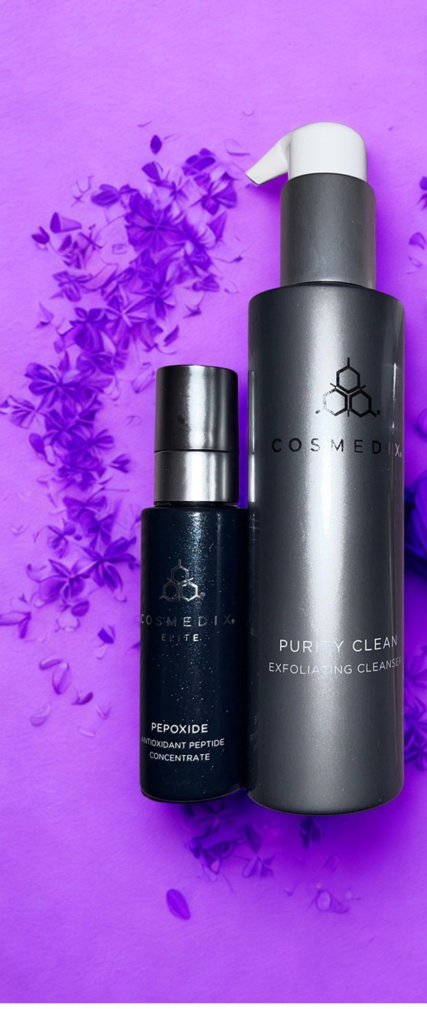 Two skincare product bottles, one labeled COSMEDIX Elite Pepoxide and the other COSMEDIX Purity Clean Exfoliating Cleanser, on a purple background with purple flowers.