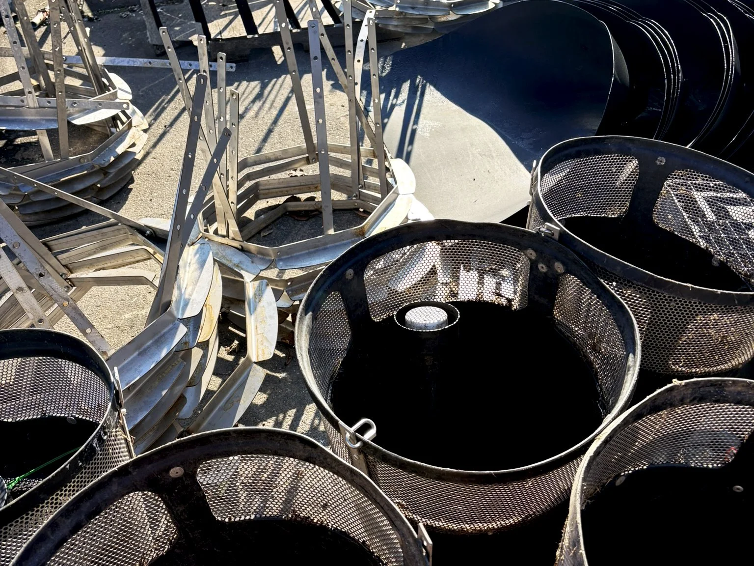 Stacked metal storm drain inserts and black plastic trash capture baskets outdoors.