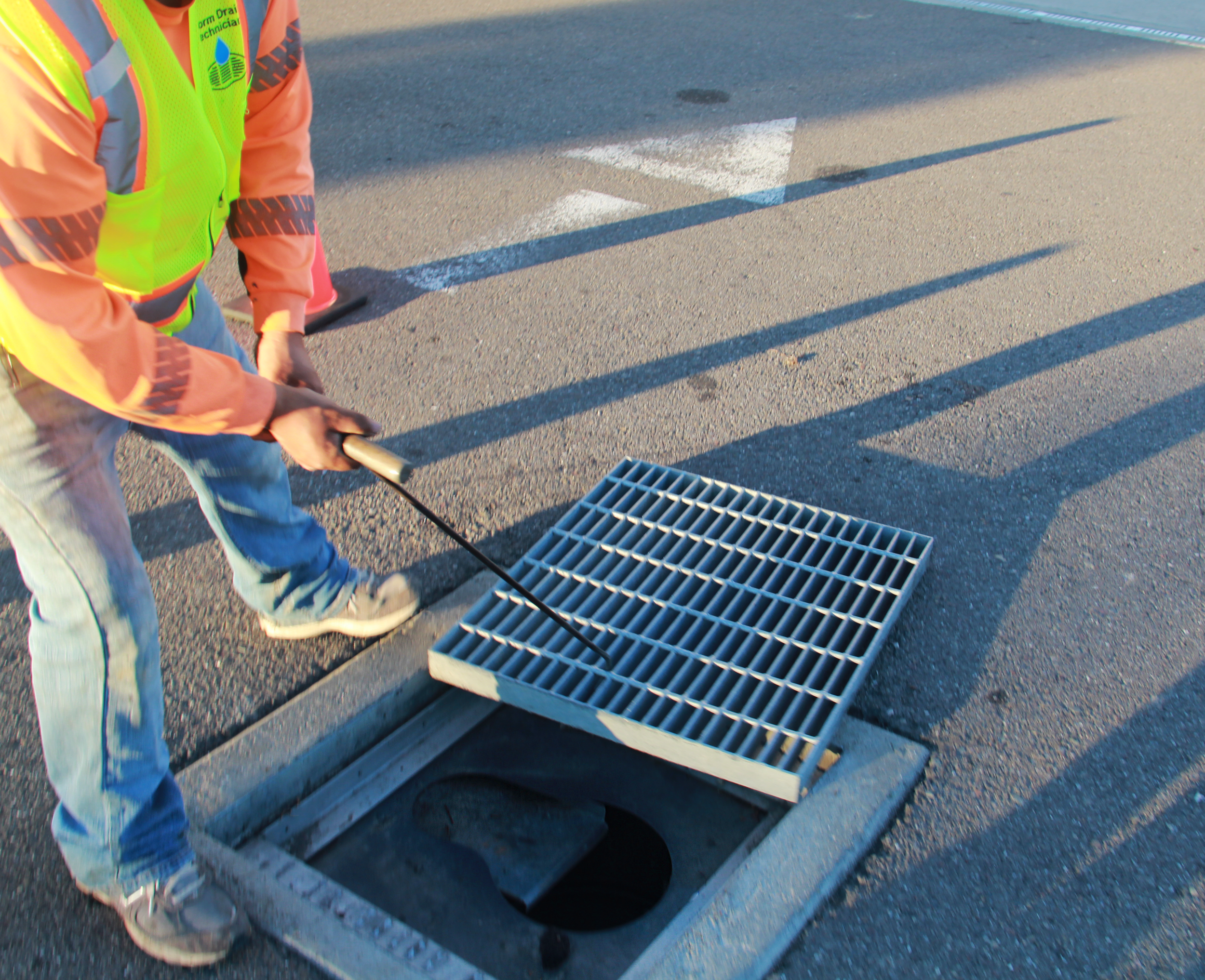 Worker in safety vest removing a storm drain grate on the street.