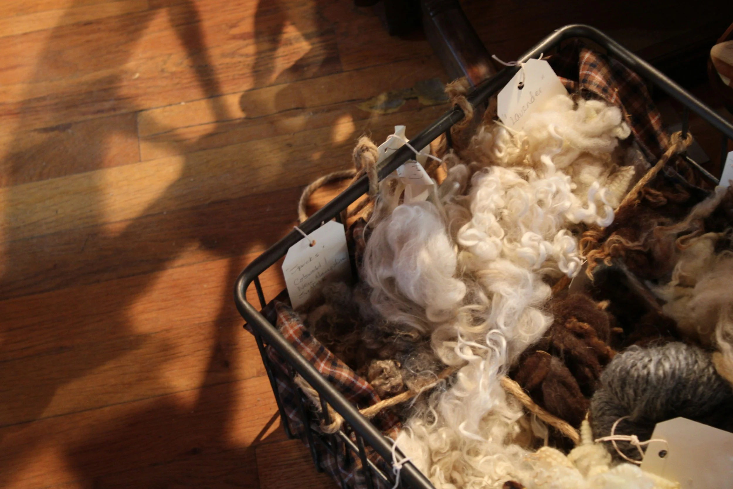A basket filled with various types of wool and fiber on a wooden floor.