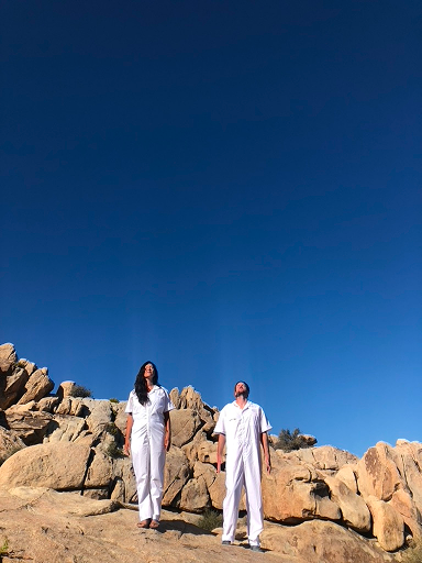 Two people wearing white standing in the desert waiting for aliens