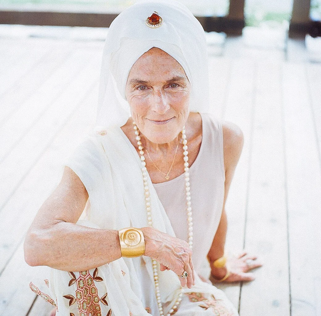 Woman in white attire with headscarf and jewelry seated on wooden platform