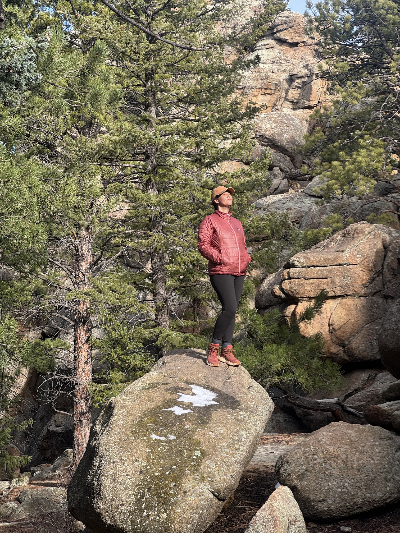 Woman standing on a rock in the mountains with the sun on her face. 