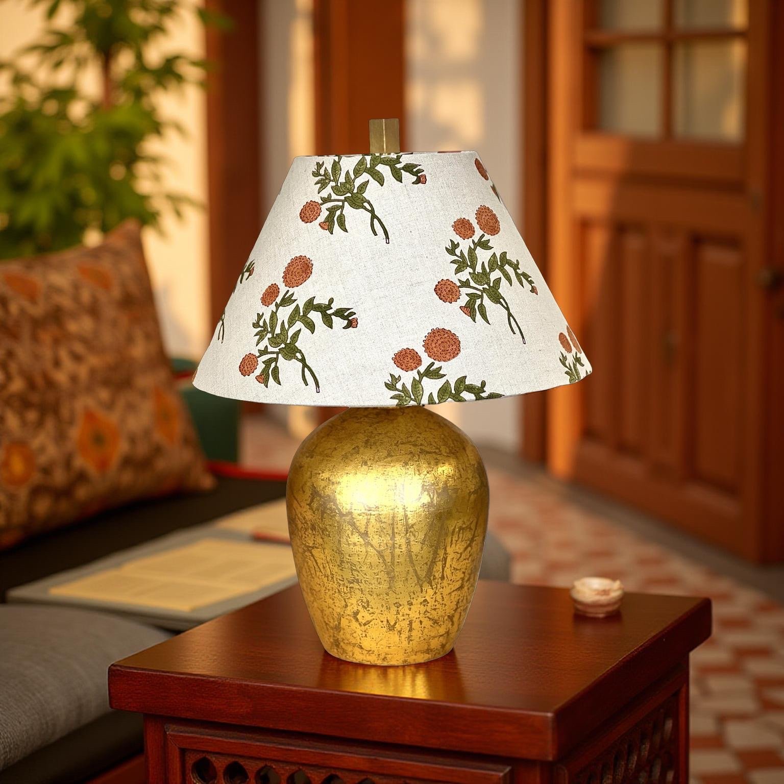 A decorative table lamp with a golden base and a white lampshade with a floral pattern of orange flowers and green leaves, placed on a wooden table.