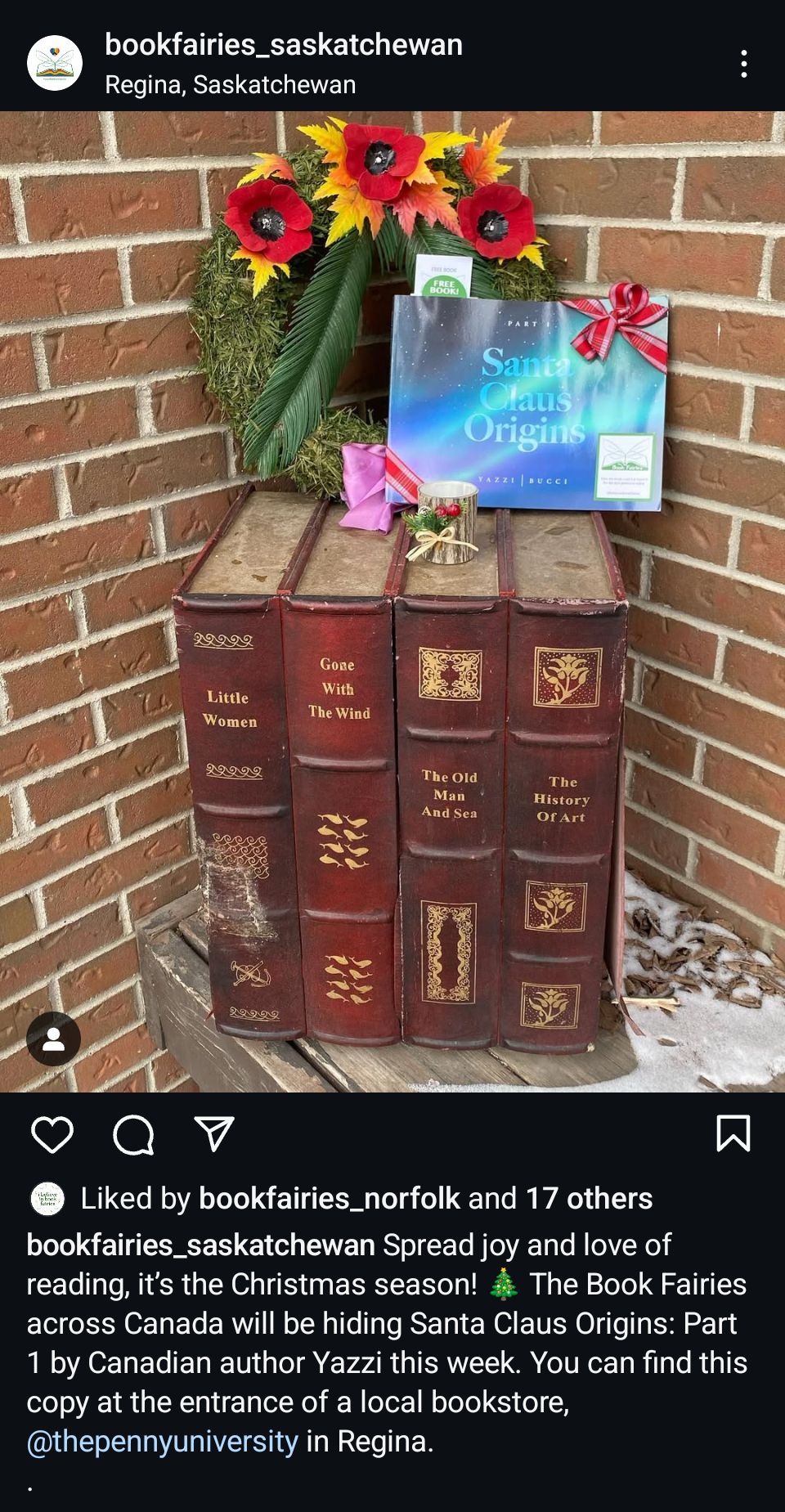 Decorative Christmas display featuring a wreath with red and yellow flowers, green leaves, and a large green palm leaf, along with a book titled "Santa Claus Origins" decorated with a red bow, a candle with holly accents, and a row of vintage-style books with titles like "Little Women," "Gone With The Wind," "The Old Man And Sea," and "The History Of Art."