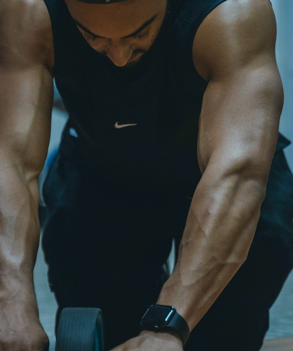 A man is lifting a dumbbell during a workout at gym, wearing a black Nike sleeveless shirt and a smartwatch on his left wrist.